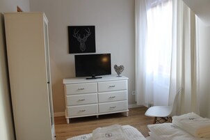 A bedroom with a white dresser, a television, a heart-shaped decoration, and a bed with white bedding.