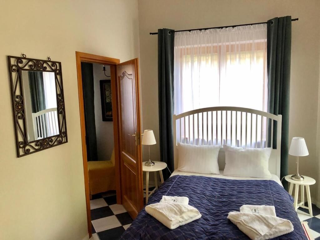 A hotel room with a bed, two bedside lamps, a mirror, a door, and a window with curtains.