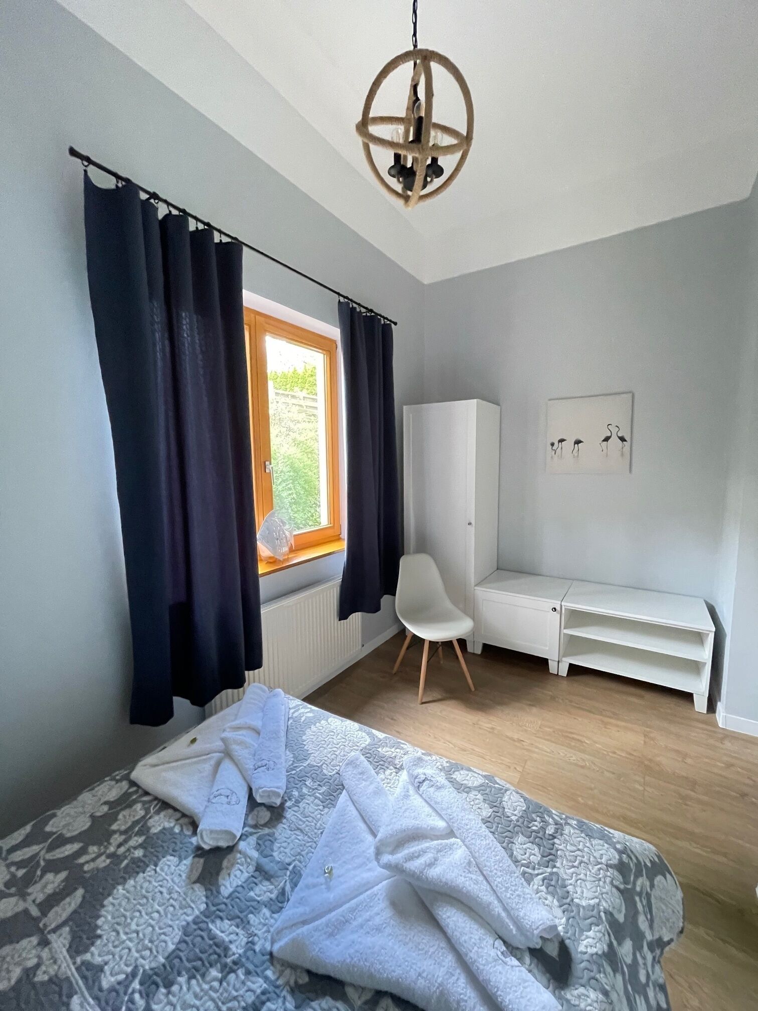 Un dormitorio con cama, una silla, armario y ventana con cortinas.