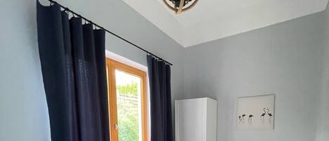 Un dormitorio con cama, una silla, armario y ventana con cortinas.