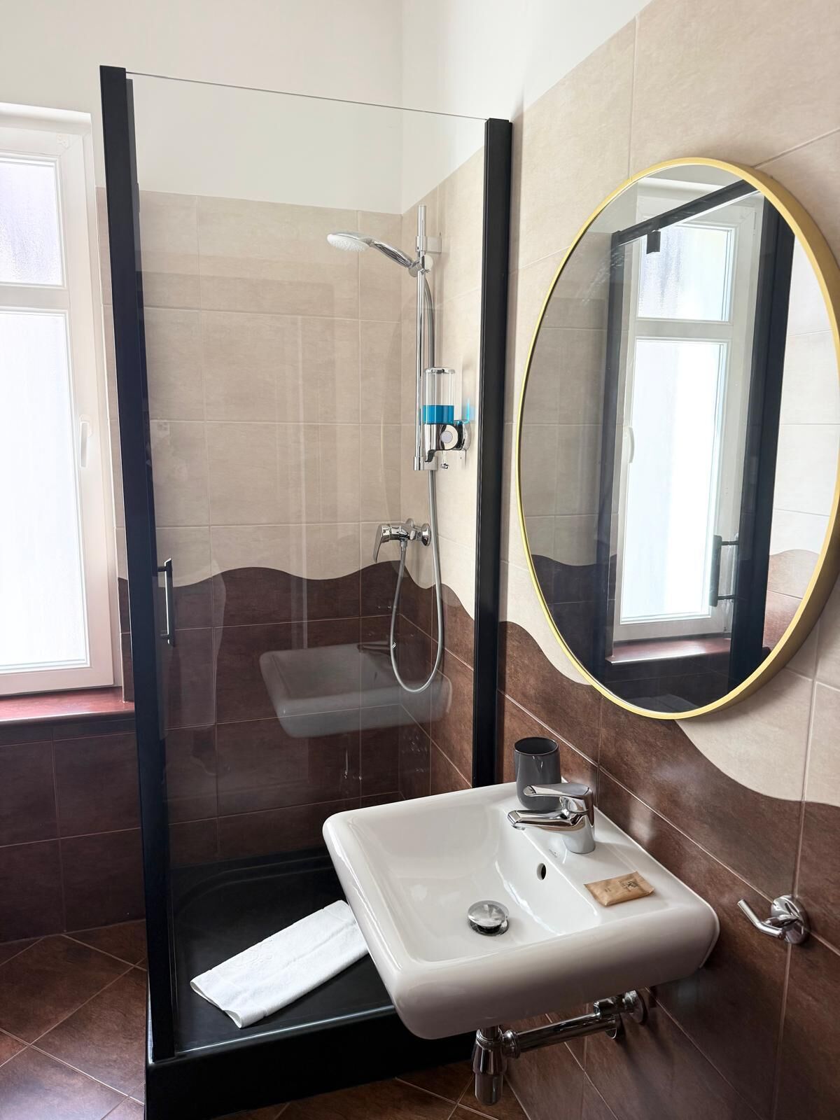 Ein modernes Badezimmer mit einer Duschkabine, einem weißen Waschbecken mit Spiegel und Blick ins Freie.