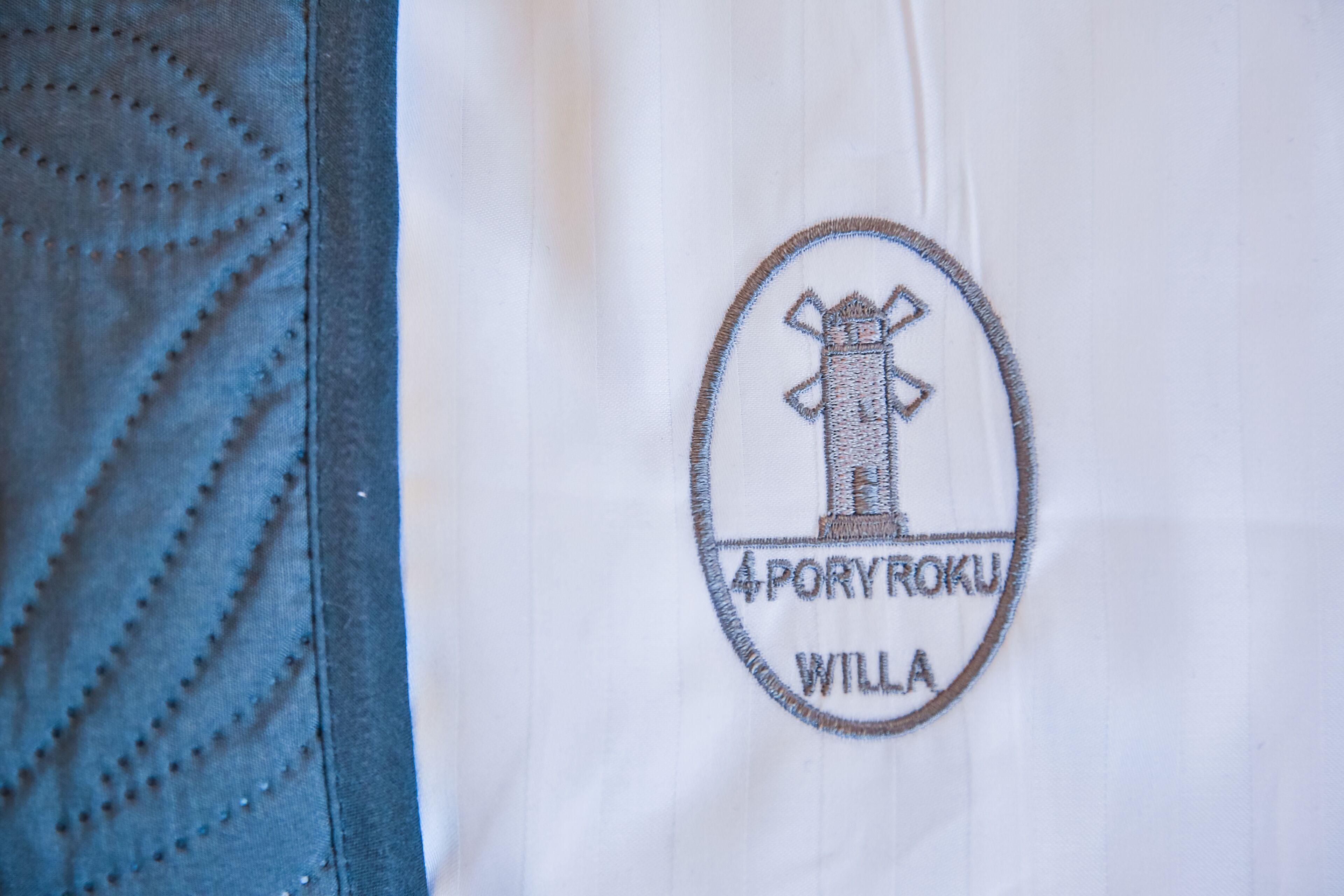 Un tissu blanc orné d’un écusson brodé représentant un bâtiment et l’inscription « 4 PORYROKU WILLA ».