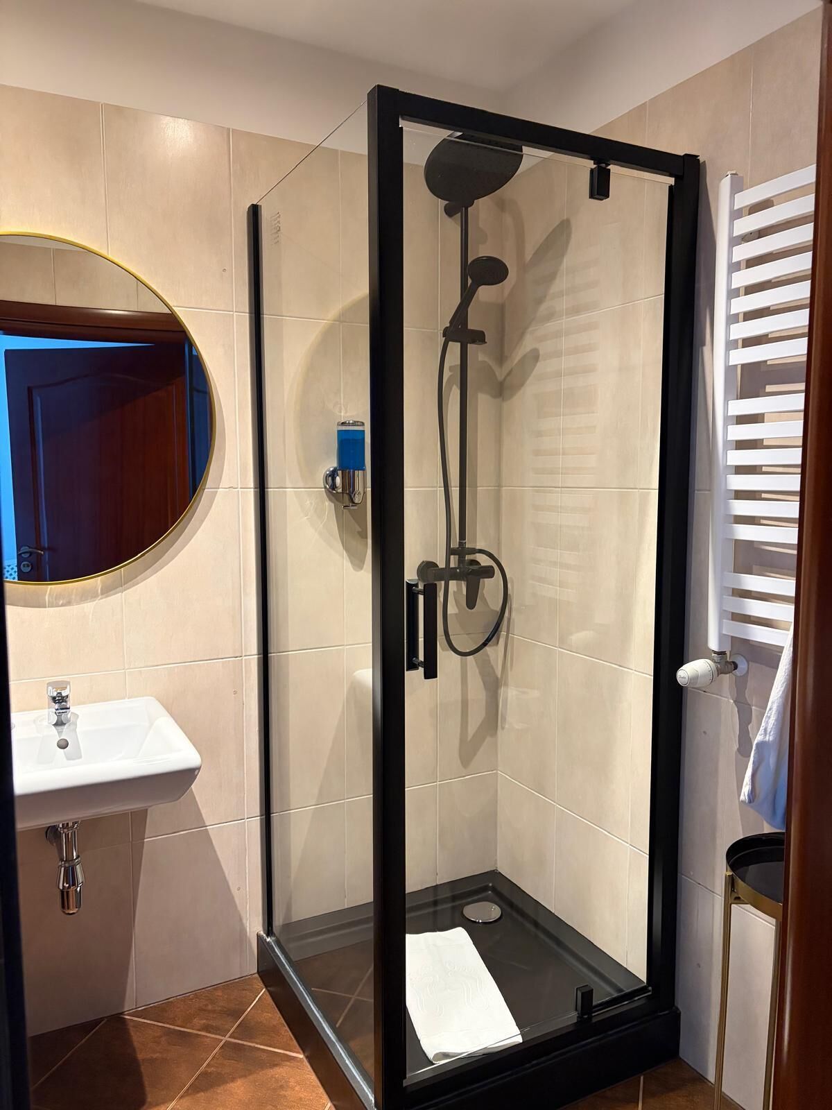 Un baño moderno con cabina de ducha de vidrio, espejo redondo y lavamanos blanco.