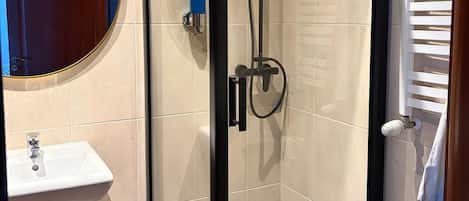 Un baño moderno con cabina de ducha de vidrio, espejo redondo y lavamanos blanco.