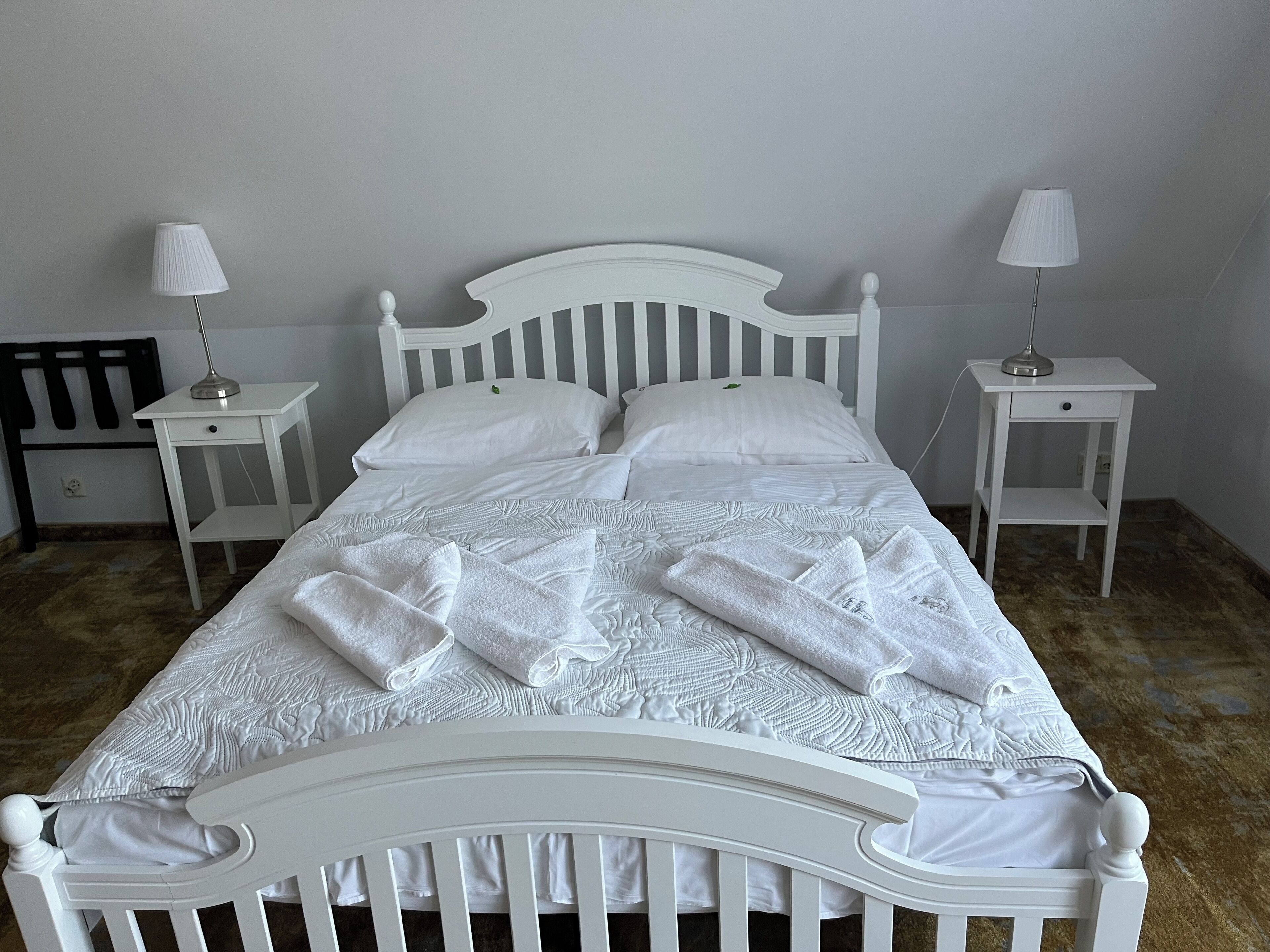 A neatly made bed with white linens and pillows, two bedside tables with lamps, and a wooden chair.