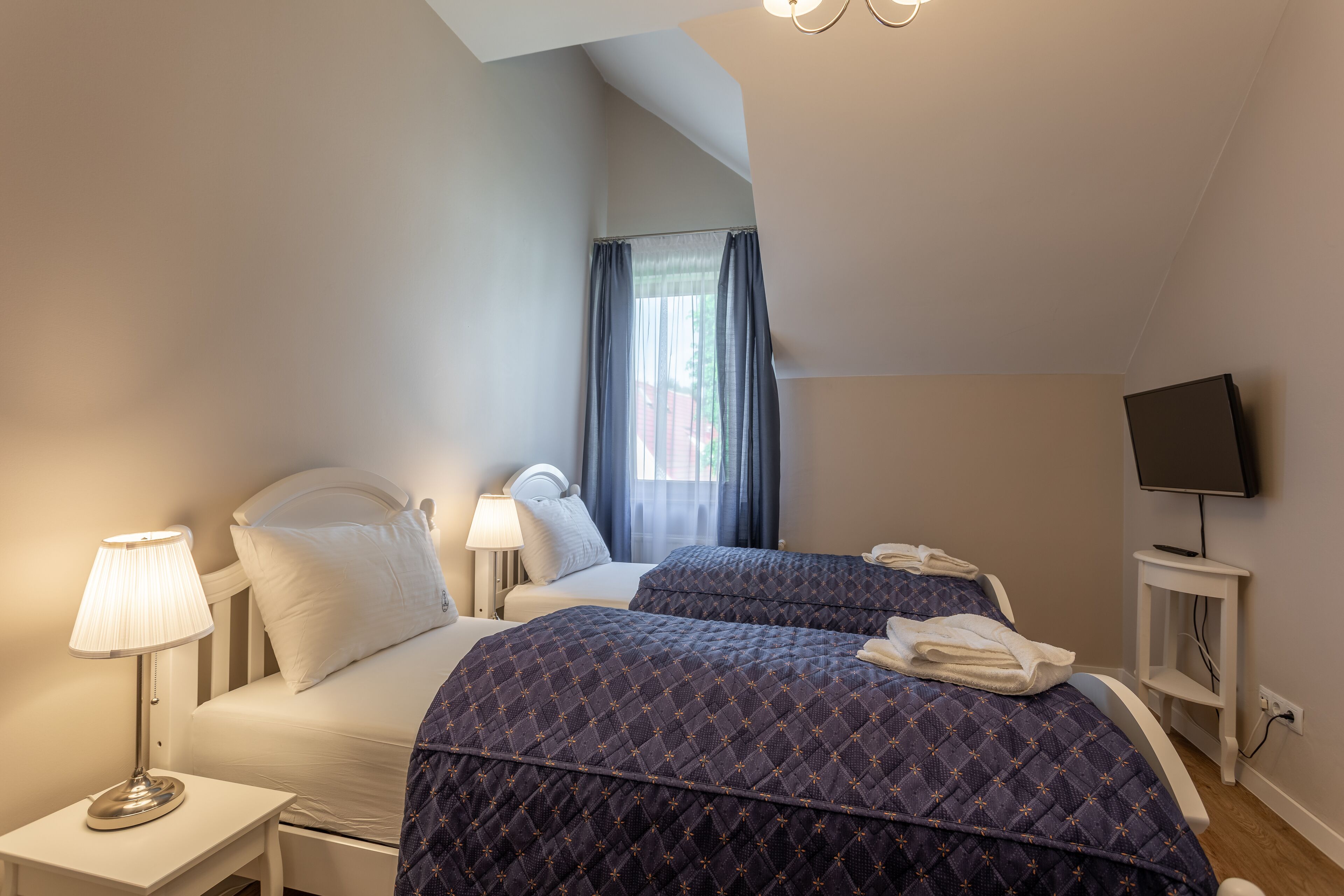A hotel room with two beds, a TV, and a lamp.