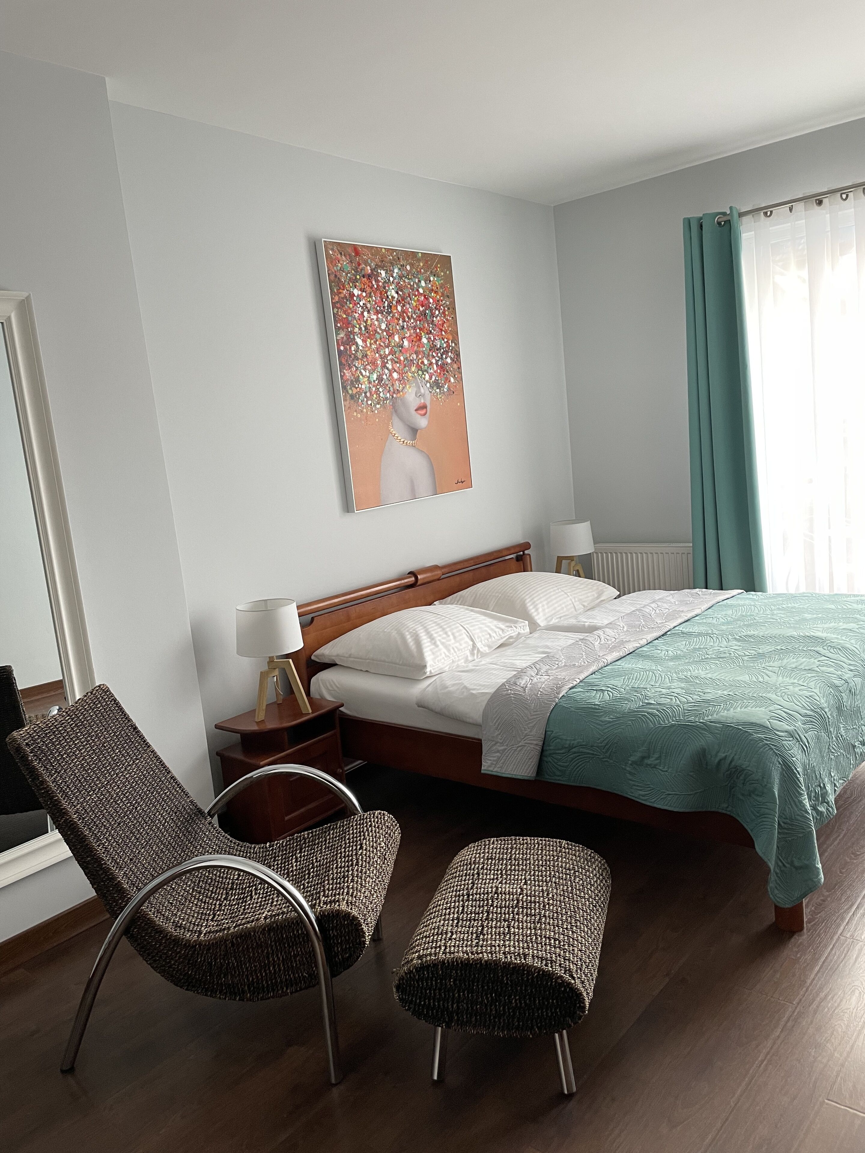 A hotel room with a bed, two chairs, a nightstand, a lamp, and a painting on the wall.