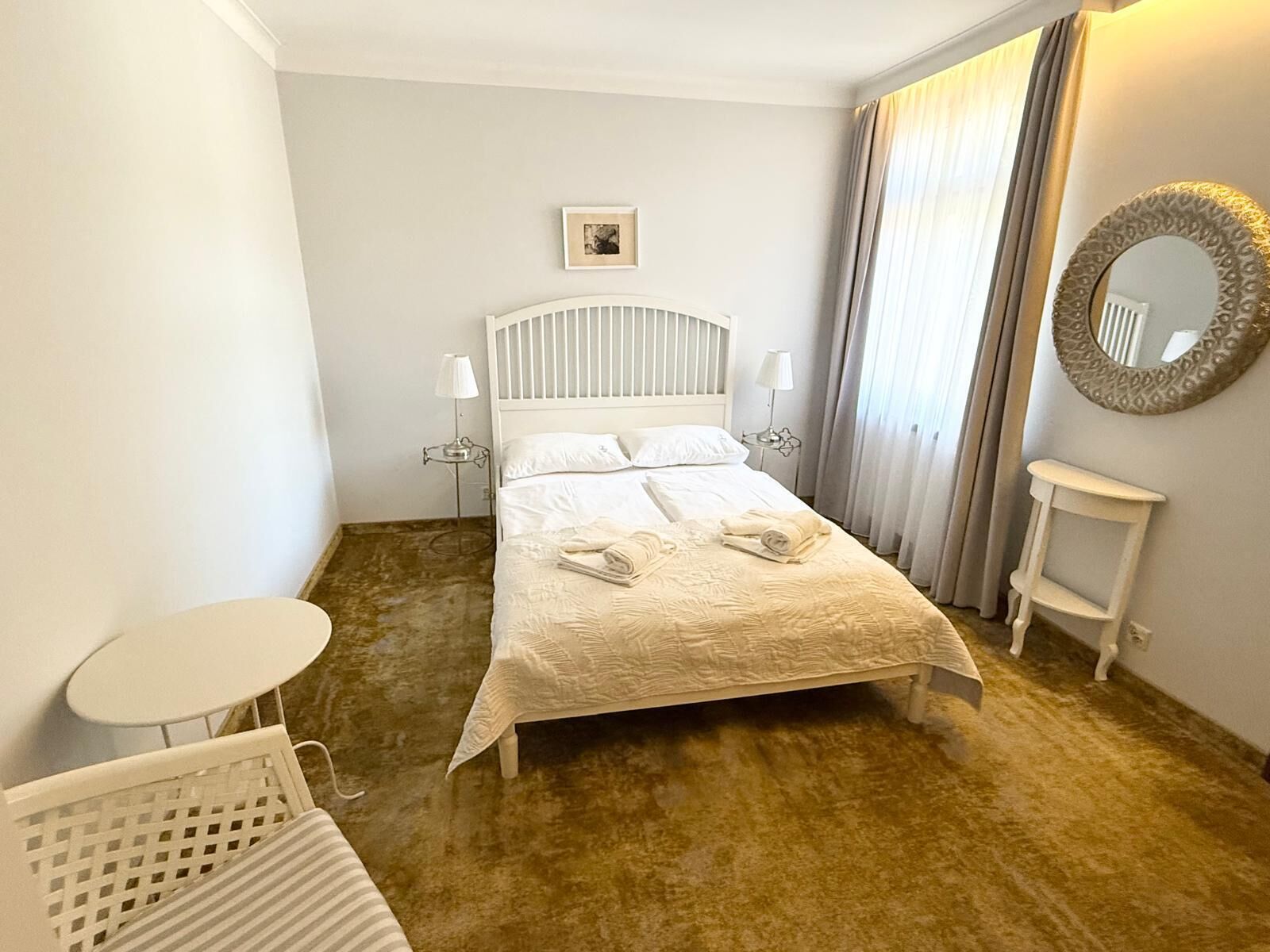 Une chambre d’hôtel avec un lit, une petite table, une chaise, une lampe de chevet et un miroir au mur.