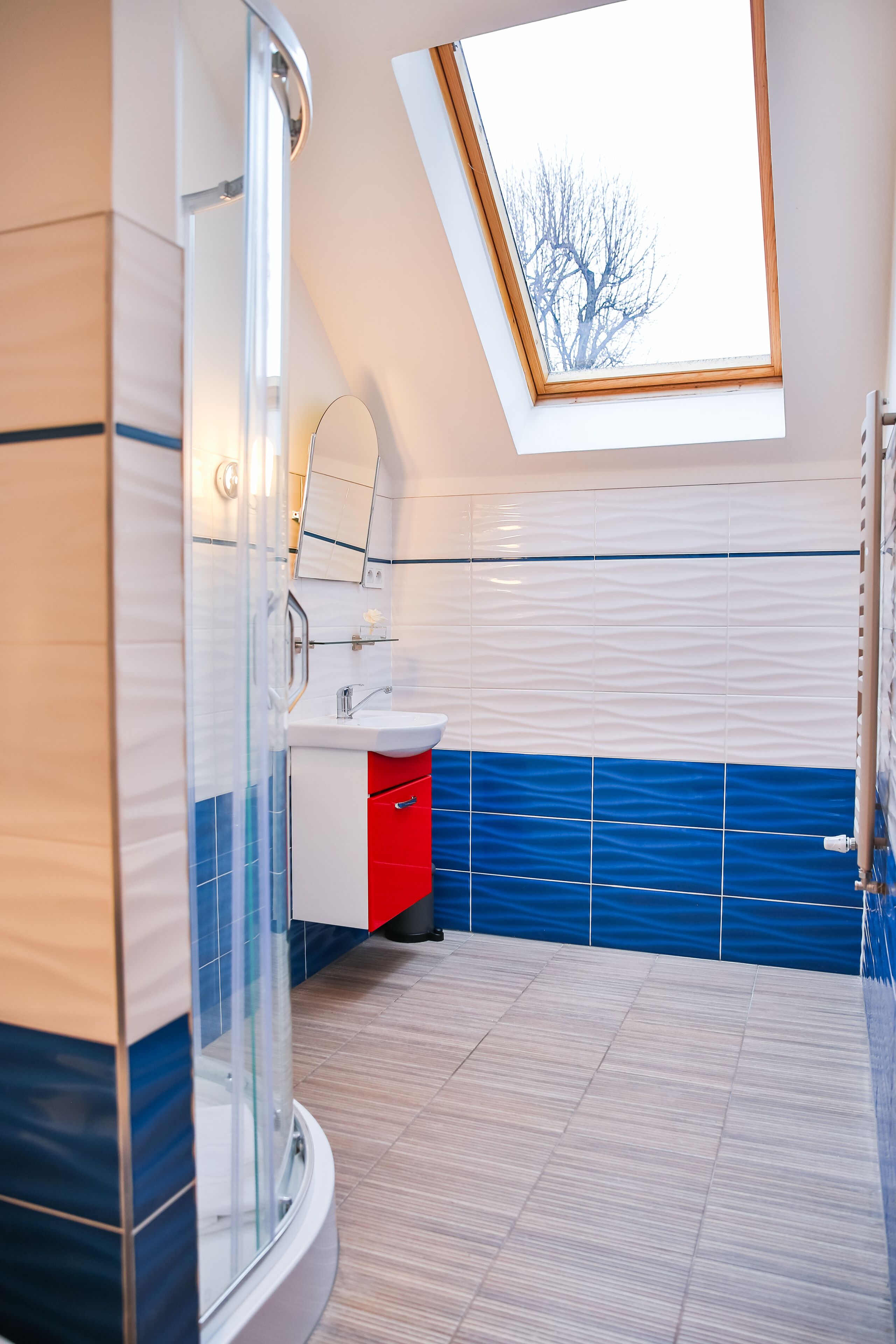 A modern bathroom with a skylight, a glass shower enclosure, and a red cabinet.