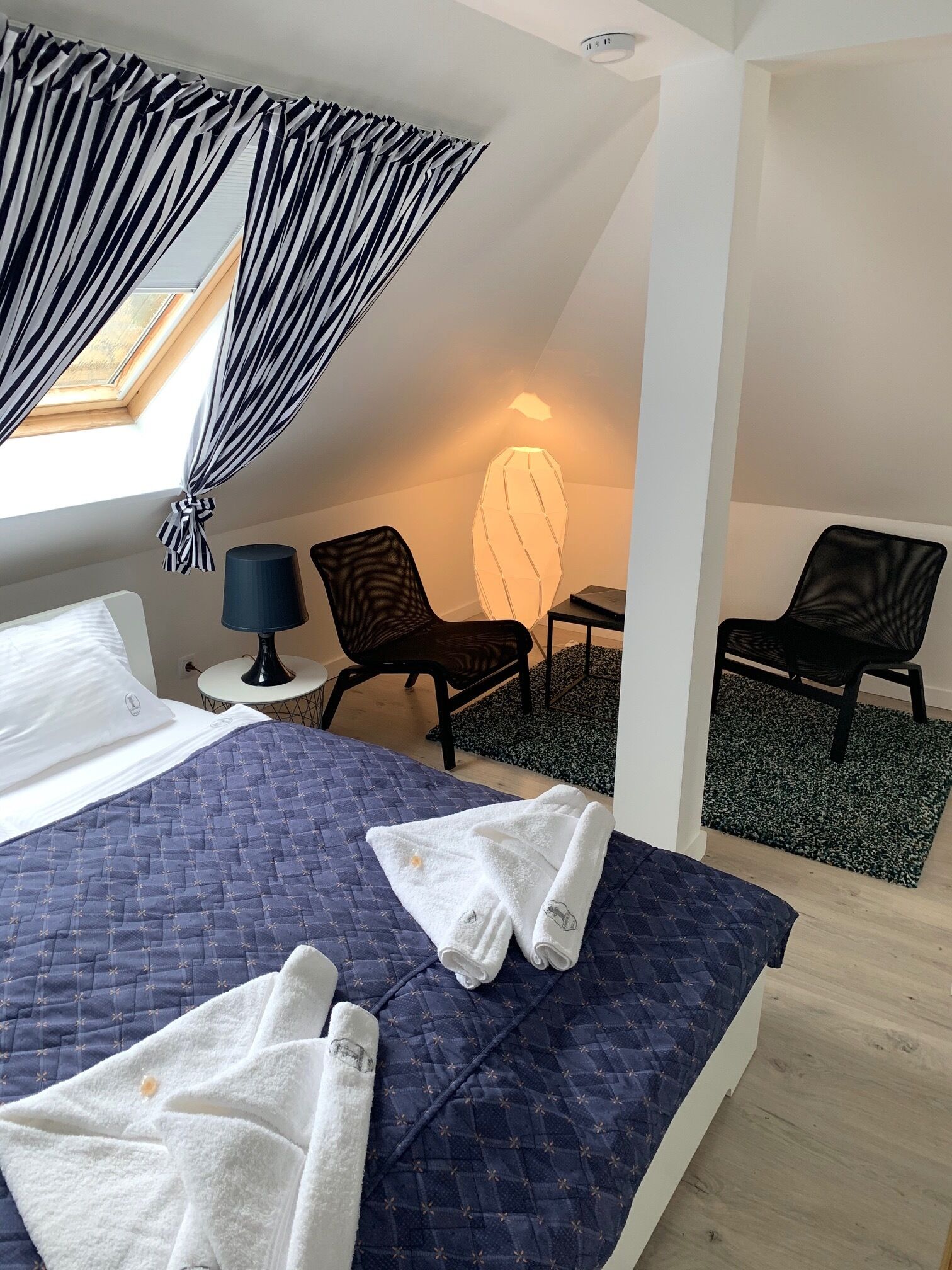 A hotel room with a bed, two chairs, a lamp, and a window with curtains.