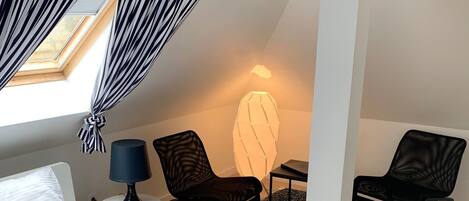 A hotel room with a bed, two chairs, a lamp, and a window with curtains.