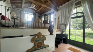 A room with a wooden ceiling, a bench with a decorative headboard, a staircase, and a large window with a view of greenery. - Guesthouse 2/4 people, 2 rooms, kitchen, bathroom, patio, A/C, pool, EV charger (San Casciano in Val di Pesa)