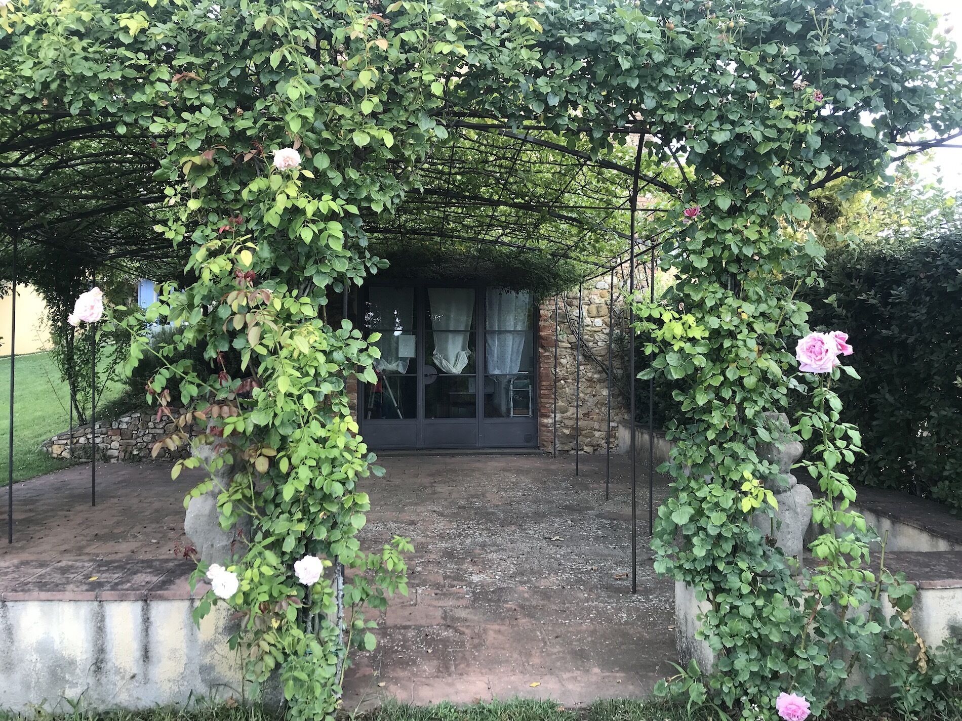 Ein überdachter Gartenbereich mit einer Steinmauer und einer Metallpergola.