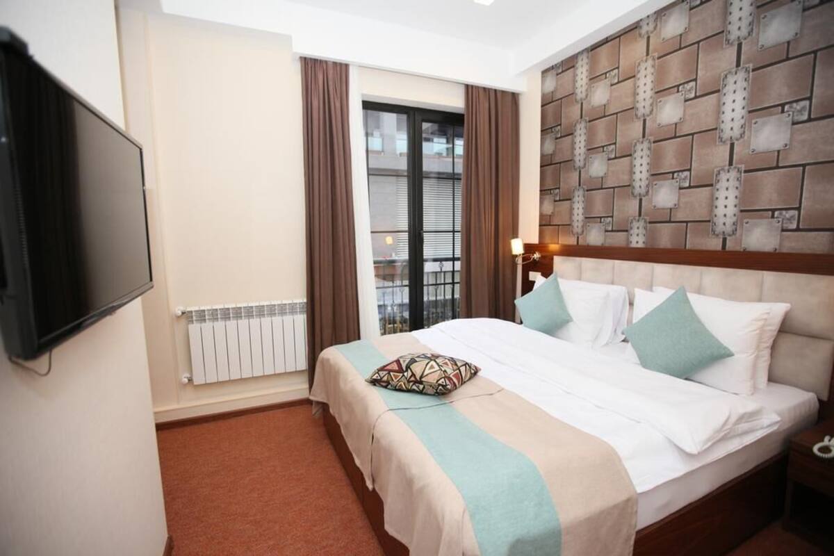 Una habitación de hotel con cama, televisor, radiador y ventana con cortinas.