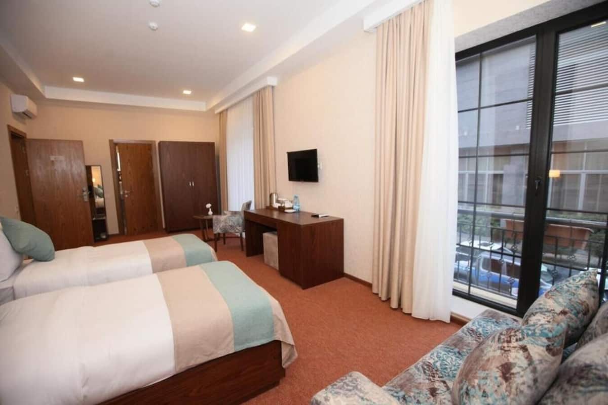 Habitación de hotel con dos camas, un escritorio, televisión y balcón con vistas.