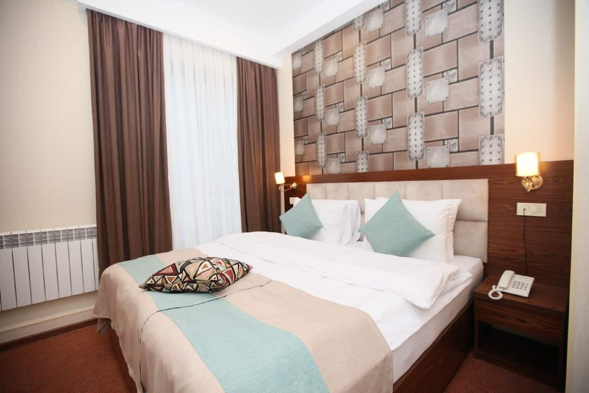 Habitación de hotel con cama, cabecera con diseño de ladrillos, mesita de noche con teléfono y ventana con cortinas.