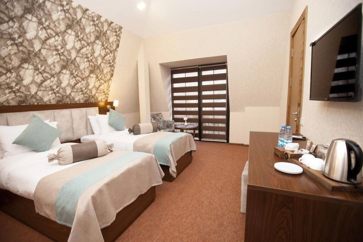 Habitación de hotel con dos camas, un escritorio de madera con tetera, televisión y ventana.