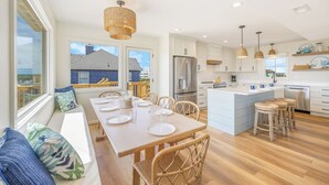 A modern kitchen with a central island, stainless steel appliances, and a view of a blue house outside. - OCEANFRONT-6 BDRM-4 Mstrs-RENOVATED 2024-Heated Pool,Hot Tub, Media & Game Rooms (Waves)
