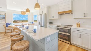 A modern kitchen with a central island, white cabinetry, and a view of the beach. - OCEANFRONT-6 BDRM-4 Mstrs-RENOVATED 2024-Heated Pool,Hot Tub, Media & Game Rooms (Waves)