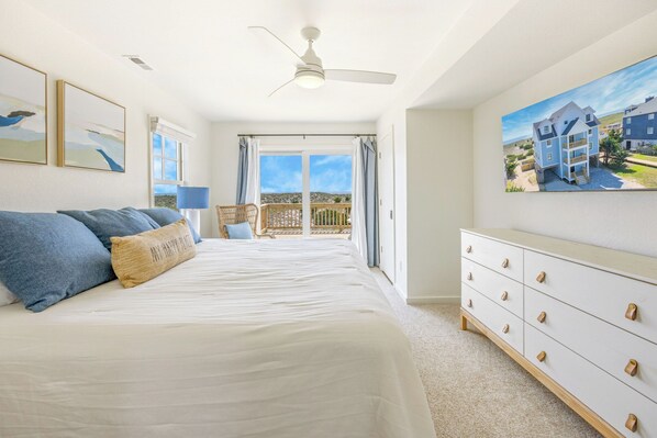 A bedroom with a large bed, a dresser, a ceiling fan, and a balcony with a view. - OCEANFRONT-6 BDRM-4 Mstrs-Heated Pool,Hot Tub, Media & Game Rooms (Waves)