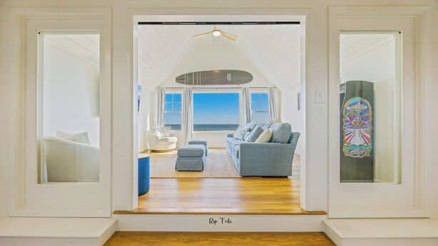A spacious living room with a view of the ocean, a ceiling fan, and a colorful skateboard decoration. - OCEANFRONT-6 BDRM-4 Mstrs-RENOVATED 2024-Heated Pool,Hot Tub, Media & Game Rooms (Waves)