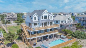 A large, multi-story house with a prominent balcony and a swimming pool. - OCEANFRONT-6 BDRM-4 Mstrs-RENOVATED 2024-Heated Pool,Hot Tub, Media & Game Rooms (Waves)