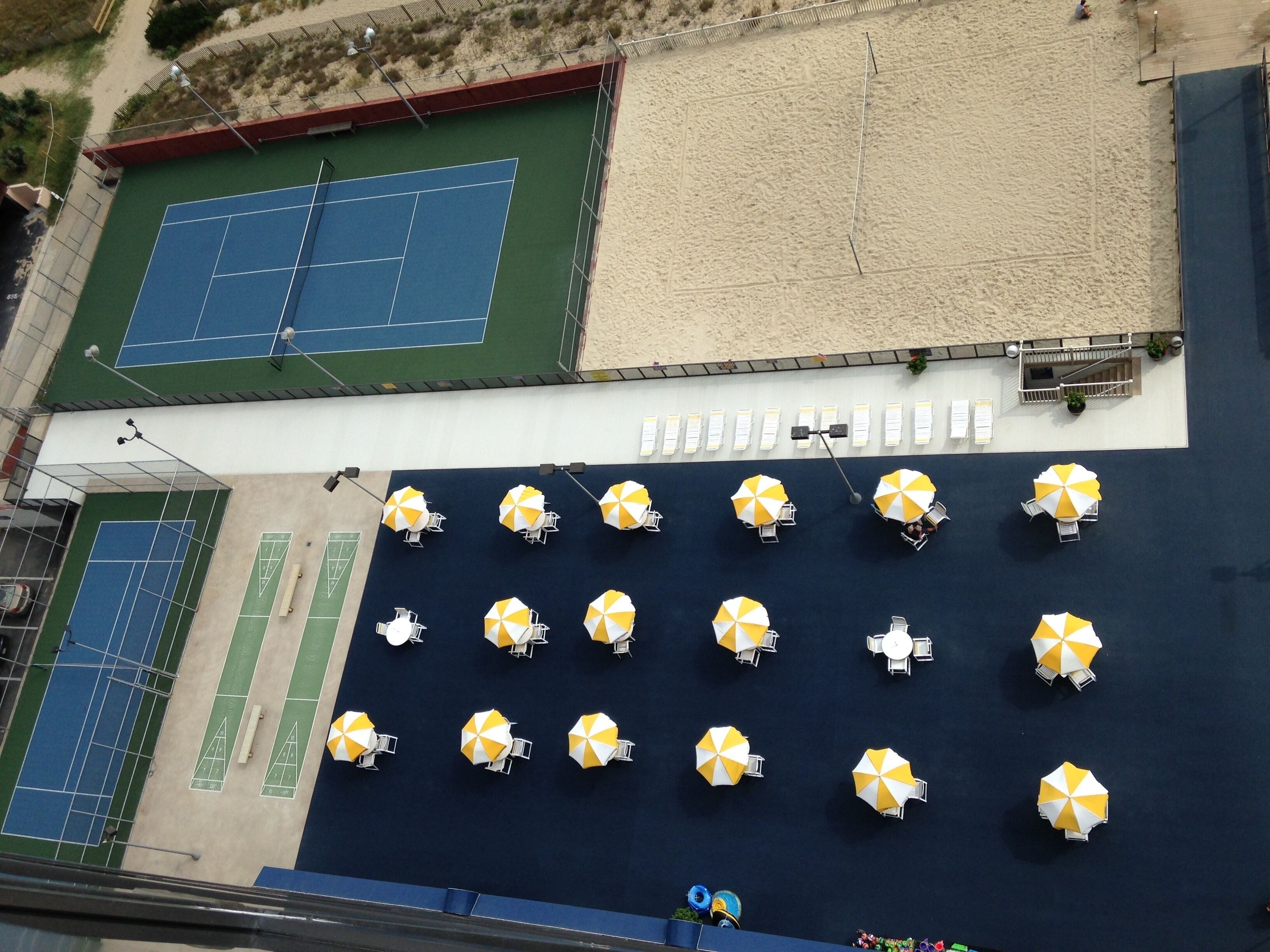 Una cancha de tenis en la azotea con varios sombrillas amarillas y blancas y zonas de estar.