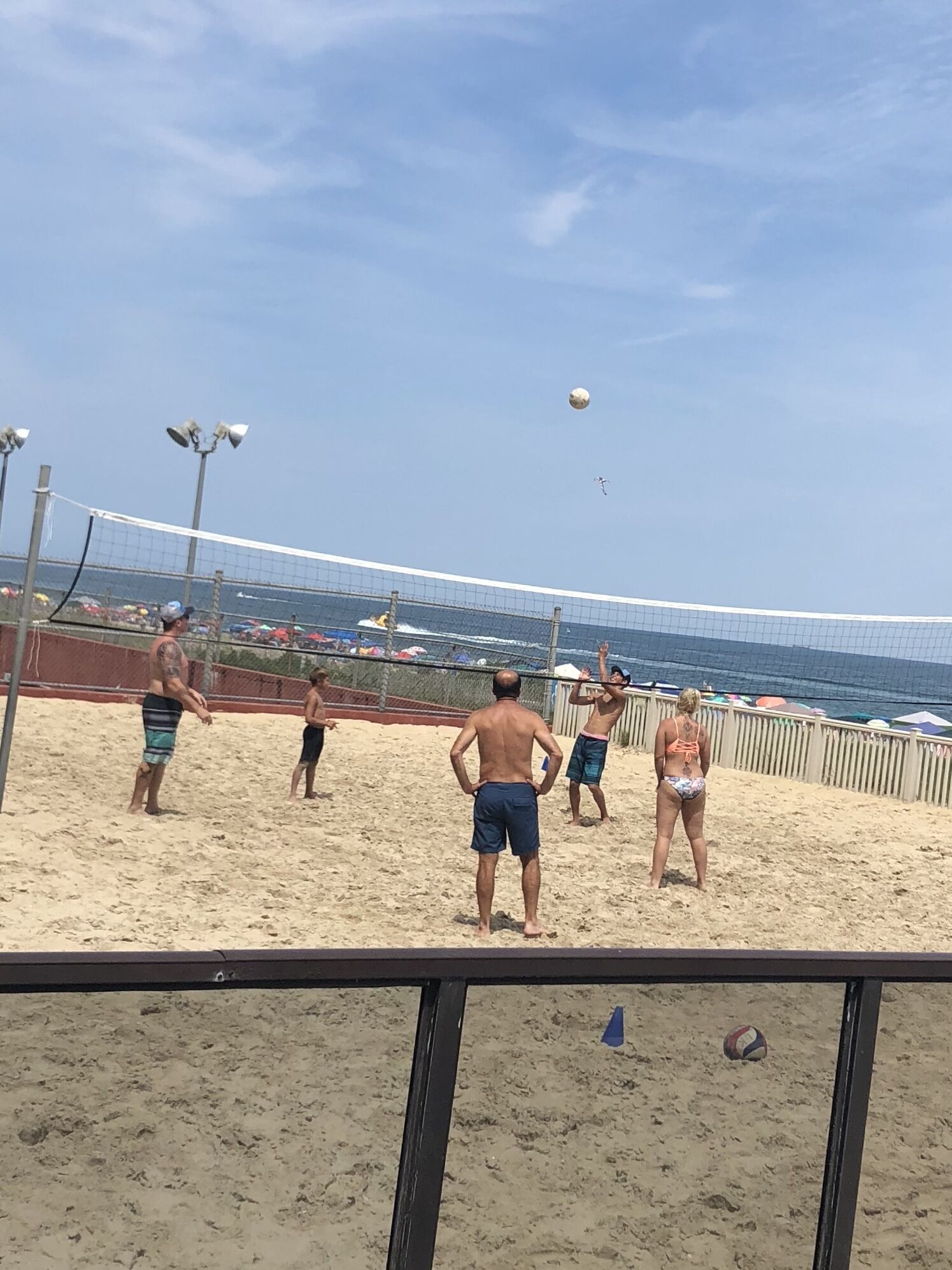 Partido de voleibol de playa con jugadores en una cancha arenosa, una red de voleibol y vista al océano en el fondo.