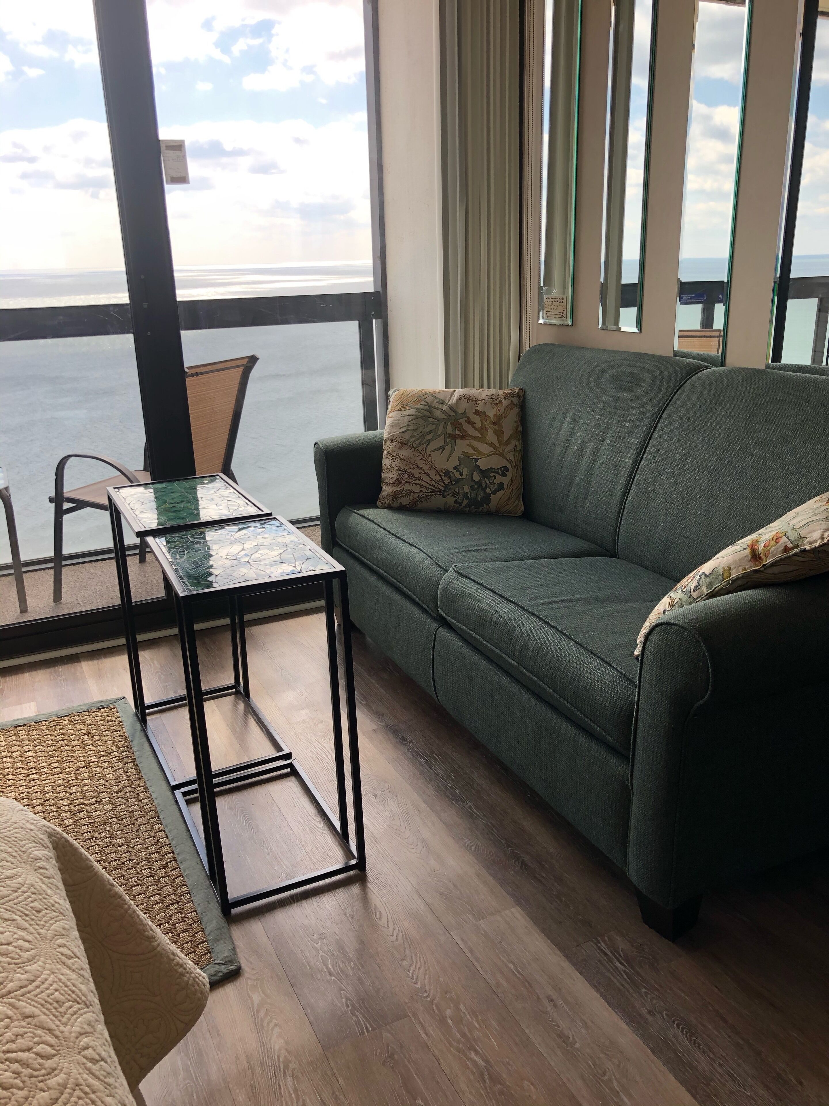 Ein modernes Wohnzimmer mit einem grünen Sofa, einem Couchtisch mit Glasplatte und Meerblick durch große Fenster.