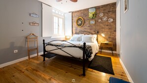 A bedroom with a bed, a wooden floor, a ceiling fan, a brick wall, and a window. - Merc Porto Downtown (Porto)