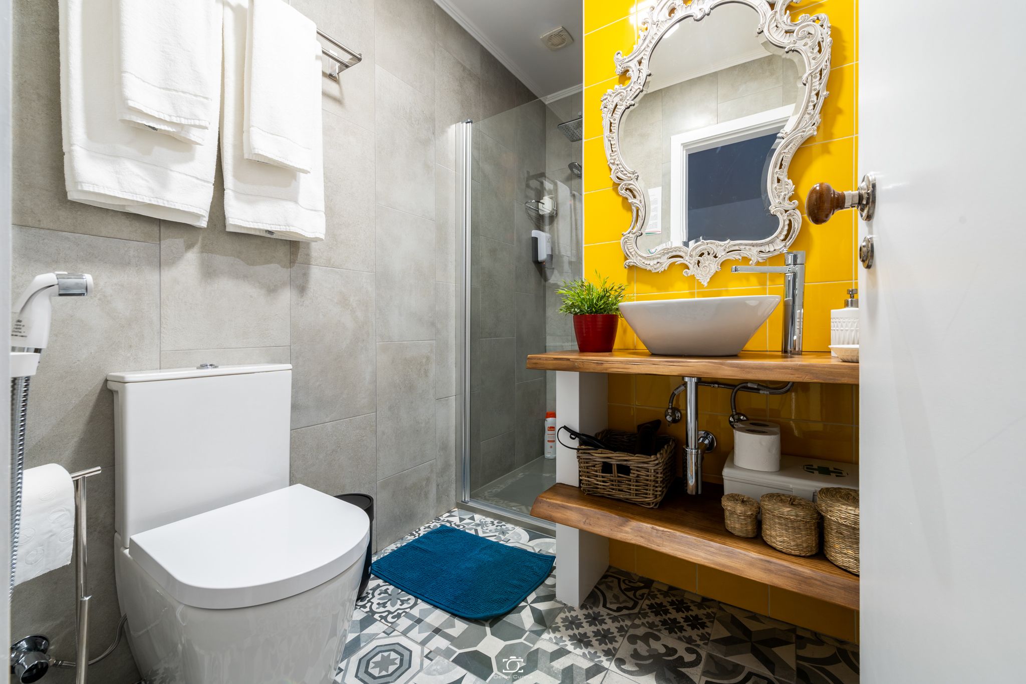 A bathroom with a toilet, a shower, a sink with a mirror, and a blue bath mat.