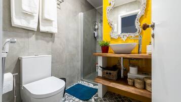 A bathroom with a toilet, a shower, a sink with a mirror, and a blue bath mat.