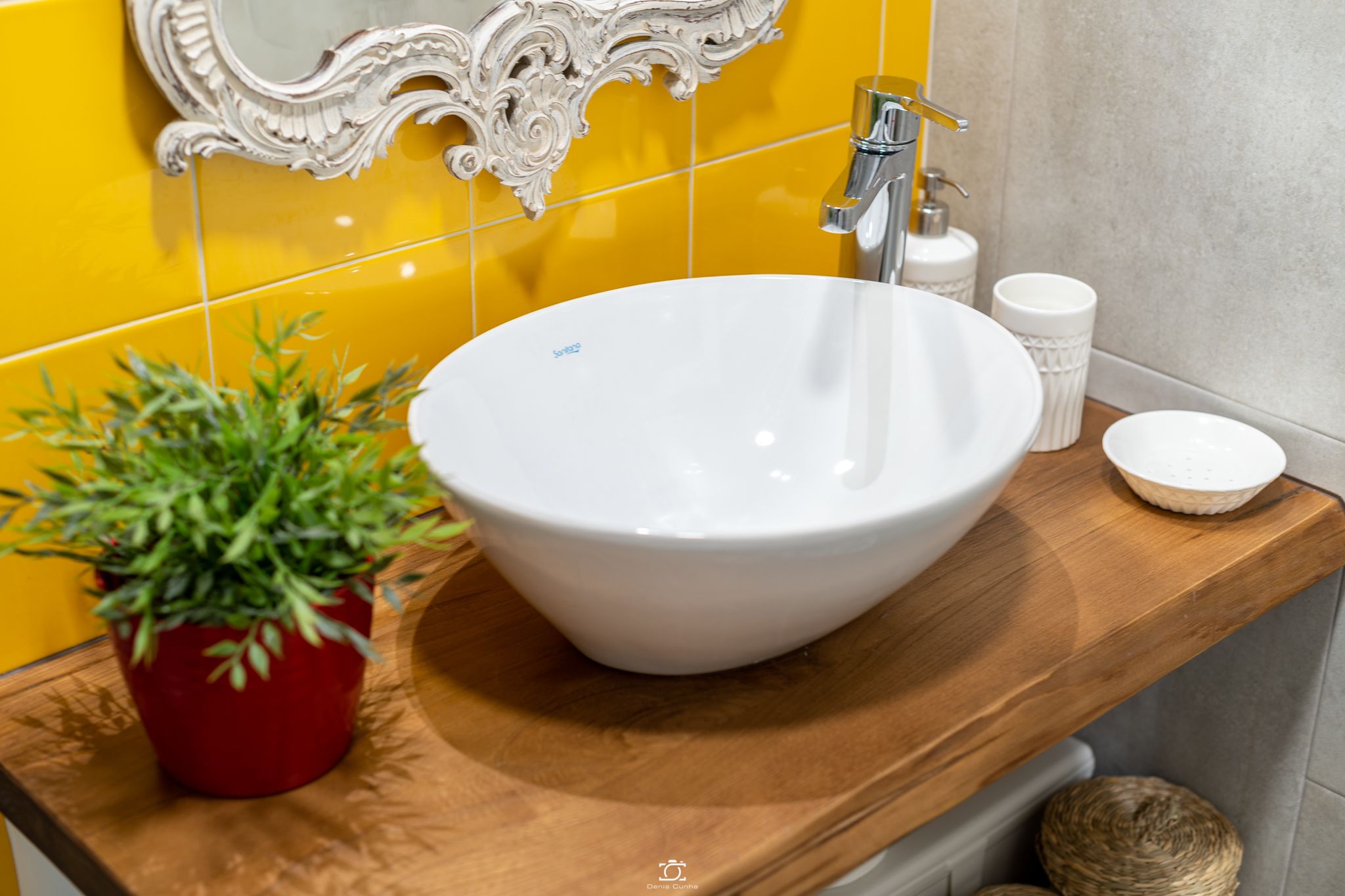 A bathroom with a white sink, a potted plant, and a mirror with ornate detailing.