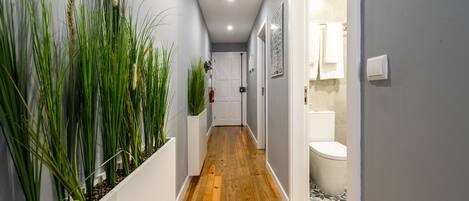 A hallway with wooden flooring, white walls, and green plants.