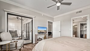 Un dormitorio con una cama grande, una silla, un escritorio y una televisión. Hay una puerta corrediza de vidrio que da a un balcón.