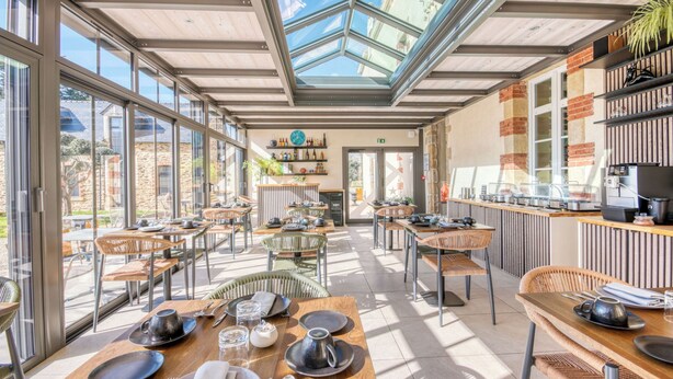 A modern restaurant with glass walls, wooden tables, and a variety of seating options.