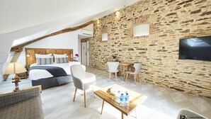 A modern hotel room with a sloped ceiling, stone wall, wooden bed, and a flat-screen TV.