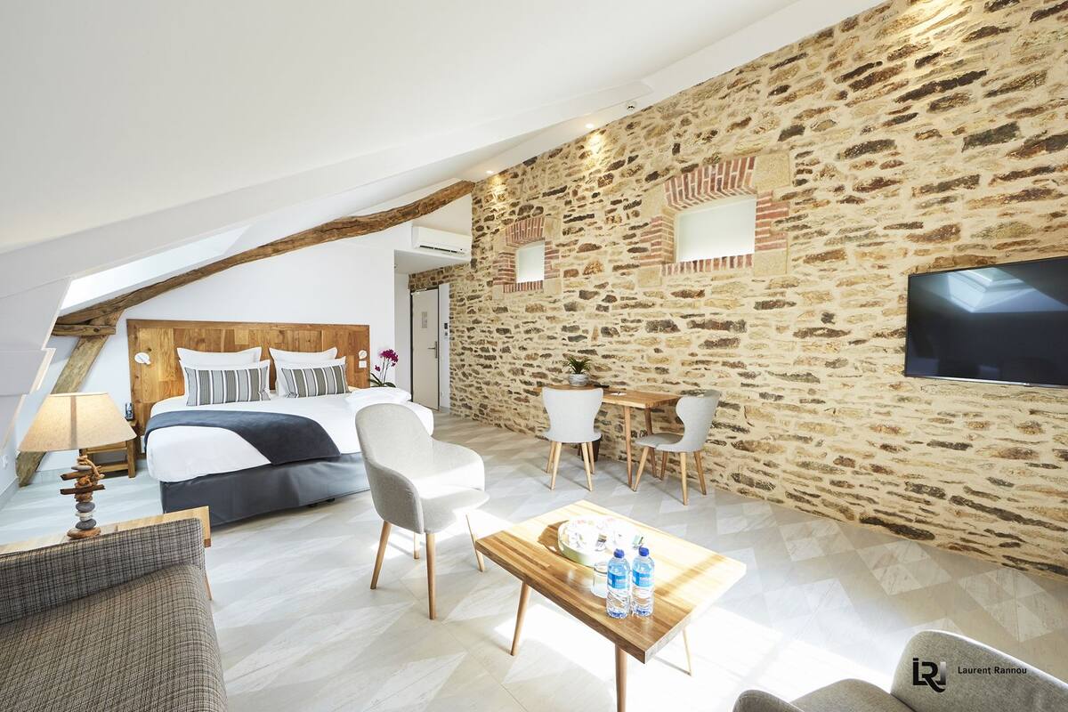 Een moderne hotelkamer met een schuin plafond, een stenen muur, een houten bed en een flatscreen televisie.