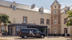 A black van parked in front of a building with a tower, a covered entrance, and outdoor seating.