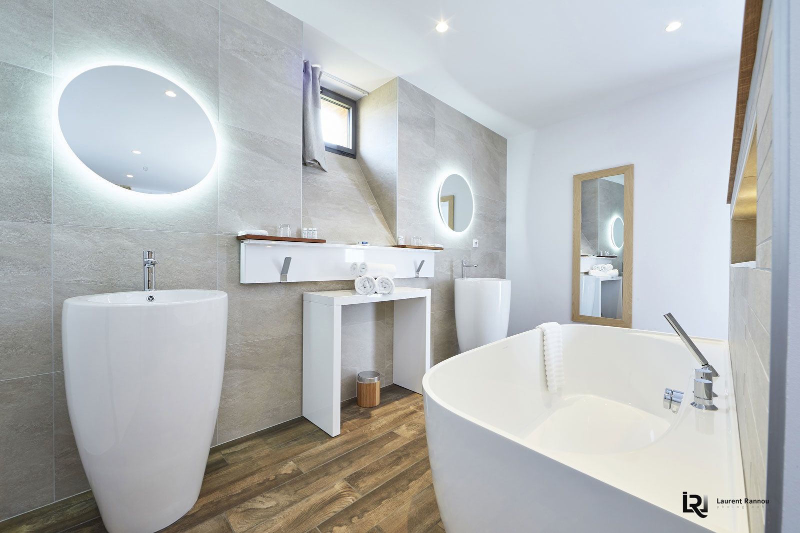 Un baño moderno con una bañera independiente, dos lavamanos y un tocador con espejo.