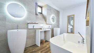 Un baño moderno con una bañera independiente, dos lavamanos y un tocador con espejo.