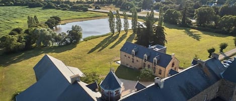 En historisk byggnad med en innergård, en damm och omgivande grönska.