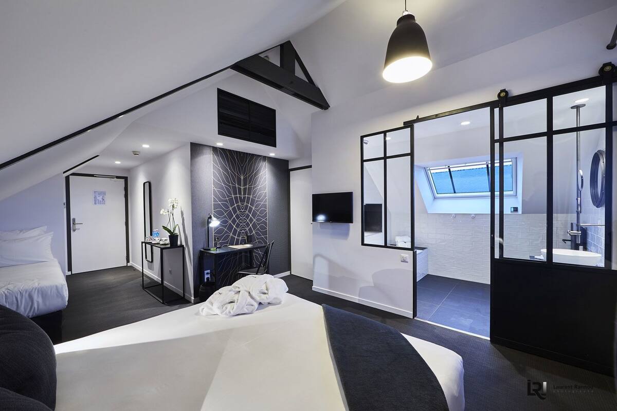 Een moderne hotelkamer met een groot bed, een bureau, een stoel, een televisie en een badkamer die zichtbaar is achter een glazen wand.