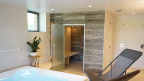 A modern bathroom with a glass-enclosed shower, a bathtub, and a lounge chair.