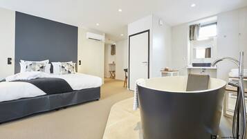 A modern hotel room with a large bed, a bathtub, and a bathroom with a sink and mirror.