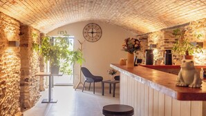 A cozy interior with a stone wall, a wooden counter with stools, and a clock on the wall.