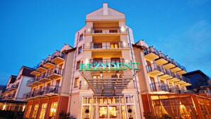 Un hotel de varios pisos con entrada central, balcones y un letrero que dice "REZIDENT".