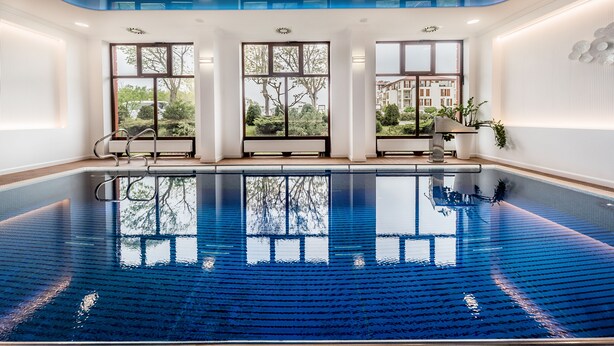 Una amplia piscina interior con paredes de vidrio transparente, que permite vistas de la vegetación y edificios circundantes.