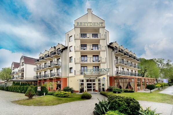 A multi-story hotel with balconies, a covered entrance, and a well-maintained garden.