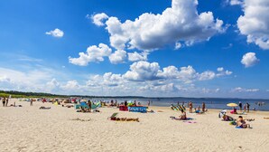 Una playa con gente tomando el sol y nadando, sombrillas y sillas de playa.